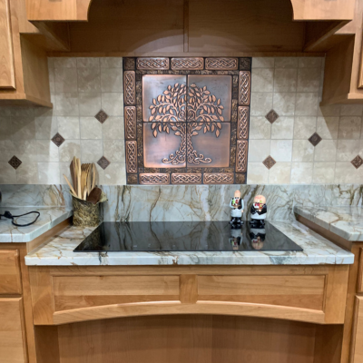 Kitchen with a marble countertop, a black stove top, ornate metal-framed backsplash above, and symmetrical diamond-pattern wall tiles behind the faucets.